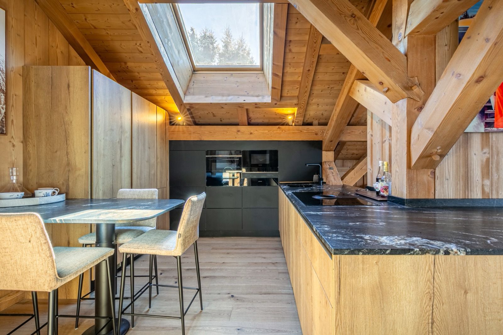 Cuisine, chalet, montagne, megève La configuration de l'appartement présentait quelques défis, notamment une cuisine de taille modeste et un conduit de cheminée mal positionné. Pour optimiser l'espace et répondre aux besoins d'un bien pouvant accueillir jusqu'à 14 personnes, nous avons imaginé une arrière-cuisine ingénieuse. Discrètement intégrée, elle offre un volume de rangement conséquent, permettant de préserver l'esthétique et la fluidité des pièces de vie principales.